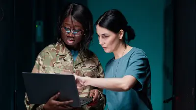 Foto von zwei Frauen in Militär-Uniform, die zusammen auf einen Laptop-Bildschirm schauen