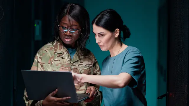 Foto von zwei Frauen in Militär-Uniform, die zusammen auf einen Laptop-Bildschirm schauen